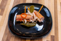 Pickled Sausage Utopenec on a black plate with pickled onion, chili strips, and bay leaves