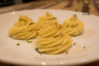 Four piped, golden-tipped Potato Kisses Bramborové Pusinky on a white plate with chive garnish.