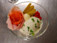 Russian Eggs (Ruské Vejce) in a glass with a ham rose, pickle spears, piped cream, and a chive-topped scoop