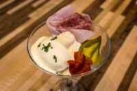 Martini glass of Russian Eggs (Ruské Vejce) with egg salad, whipped sauce, ham, roasted pepper, and pickle.