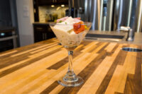 Russian Eggs (Ruské Vejce) layered in a martini glass with diced ham and herb garnish on a wood counter.