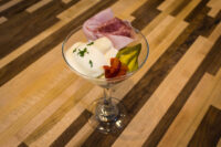 Russian Eggs (Ruské Vejce) in a martini glass with ham draped over the rim, pickle, and bacon garnish.