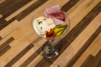 Russian Eggs (Ruské Vejce) in a stemmed glass with egg salad scoops, ham, pickle, and herb garnish.