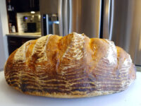 A round loaf of Rustic Bread or Baguettes with a scored, flour-dusted crust on a white counter.