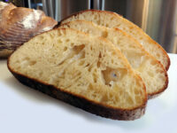 Three slices of Rustic Bread or Baguettes showing open crumb, with the whole loaf behind them
