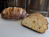 Whole scored loaf of Rustic Bread or Baguettes beside sliced pieces showing open crumb.