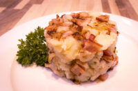 Rustic Crushed Potatoes with Bacon and Onion Round mound of Rustic Crushed Potatoes with Bacon and Onion topped with crispy bacon, plated with parsley.