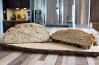 Czech Rye Bread loaf sliced in half, showing speckled crumb, on a bark-edged wooden board.