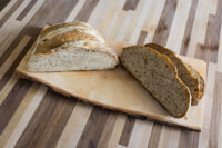 Halved loaf of Czech Rye Bread with several slices cut on a wooden board.