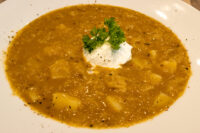 Bowl of Czech Sauerkraut Soup Zelňačka with diced potatoes, sour cream dollop, and parsley garnish.