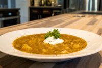 Bowl of Czech Sauerkraut Soup Zelňačka with diced potatoes, sour cream, and parsley on a wood counter.