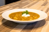 Bowl of Czech Sauerkraut Soup Zelňačka with diced potatoes, sour cream, and parsley on a wooden table.