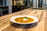 White bowl of Czech Sauerkraut Soup Zelňačka with orange broth, diced pieces, sour cream, and parsley on a wood counter.