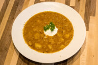 Bowl of Czech Sauerkraut Soup Zelňačka with diced potatoes, sour cream dollop, and parsley on a wooden table.