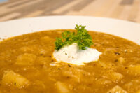Bowl of Czech Sauerkraut Soup Zelňačka with sour cream dollop and parsley garnish, potato chunks visible.