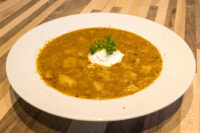 Bowl of Czech Sauerkraut Soup Zelňačka with diced potatoes, sour cream, and parsley on a wooden table