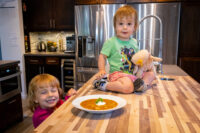Bowl of Czech Sauerkraut Soup Zelňačka with sour cream and parsley on a wooden counter, children nearby.