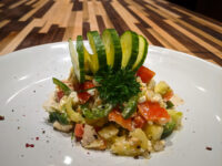 Shopska Salad Shopska Salad with diced tomato, cucumber, and feta, topped with a cucumber fan and parsley on a white plate.