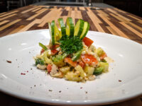 Shopska Salad Diced tomato, cucumber, and feta Shopska Salad garnished with cucumber ribbons on a white plate.