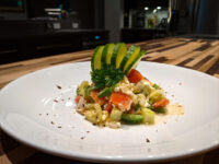 Shopska Salad Shopska Salad with diced tomato and feta, plated with a fanned avocado garnish and parsley.