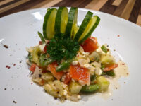 Shopska Salad Plated Shopska Salad topped with a folded cucumber fan and a sprig of curly parsley.