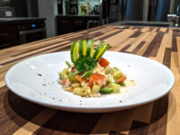 Shopska Salad Diced Shopska Salad on a white plate, topped with a cucumber ribbon fan and herb sprig, on a striped wood counter.