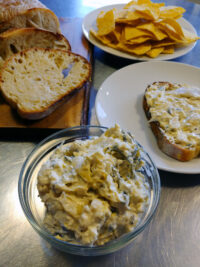 Glass bowl of Artichoke Spinach Dip with bread slices, tortilla chips, and dip on toast.