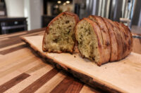 Sliced Twice-baked Herb Bread loaf on a wooden board, showing herb-flecked crumb and crisp crust.