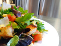 Close-up of Vinaigrette Salad with mixed greens, diced tomato, corn, shaved cheese, and croutons on a white plate