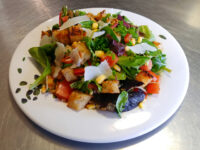 Vinaigrette Salad with greens, tomato, corn, shaved parmesan, and croutons on a white plate.