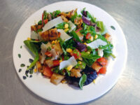 Vinaigrette Salad with greens, tomato, corn, shaved cheese, and croutons on a leaf-patterned white plate.