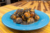 Pile of Bobalky with Poppyseeds and Honey, dough balls coated in poppyseeds on a blue plate.