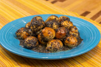 Bobalky with Poppyseeds and Honey piled on a blue plate, some balls dark with poppyseed, pooled honey beneath