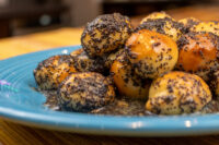 Pile of Bobalky with Poppyseeds and Honey, poppy-seed-coated dough balls glazed in syrup on a blue plate.