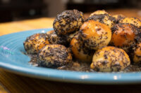 Round Bobalky with Poppyseeds and Honey, glossy and poppy-seed coated, piled on a teal plate.