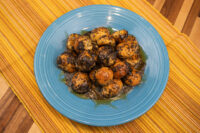 Bobalky with Poppyseeds and Honey piled on greens, glossy with honey, on a blue plate over an orange striped mat.