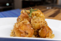 Golden bobalky dumplings piled high, topped with sauerkraut and a rosemary sprig on a white plate.