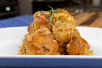 Pile of golden bobalky bun pieces topped with strands of sauerkraut and a rosemary sprig on a white plate.