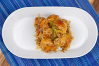 Golden bobalky dumplings topped with sauerkraut and a herb sprig, served on a white oval plate.