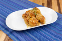 White oval plate of Bobalky with Sauerkraut, rounded buns coated in glossy sauerkraut, herb garnish, blue mat.