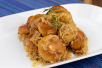 Golden bobalky with sauerkraut piled on a white plate, garnished with a rosemary sprig.