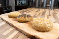 Three seed-topped bagels, two with sesame and one with poppy seeds, resting on a wooden board.
