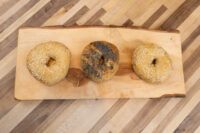 Three bagels, two with sesame seeds and one dark-seeded, on a live-edge wooden board.