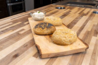Three topped Bagels -- poppy seed, sesame seed, and mixed seed -- on a wooden board with a bowl of cream cheese.