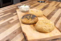Bowl of Creamy Spread with Garlic and Chives beside seeded bread rolls on a wooden board.