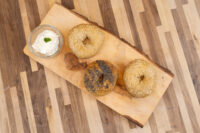 Three bagels, two with sesame seeds and one with poppy seeds, rest on a wooden board beside cream cheese.