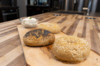 Three Bagels—poppy seed, sesame seed, and plain—on a wooden board beside a bowl of cream cheese.