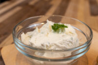 Glass bowl of Creamy Spread with Garlic and Chives, whipped and garnished with a parsley sprig, on wood