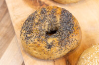 A poppy seed-topped bagel with a center hole resting on a wooden board.