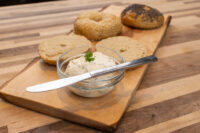 Sesame and poppy seed bagels, halved bagel, and a bowl of cream cheese on a wooden board.